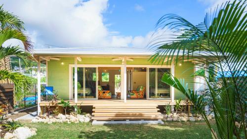a green house with a porch and palm trees at Villa UUJI-KAZE ヴィラ ウージ カゼ in Nanjo