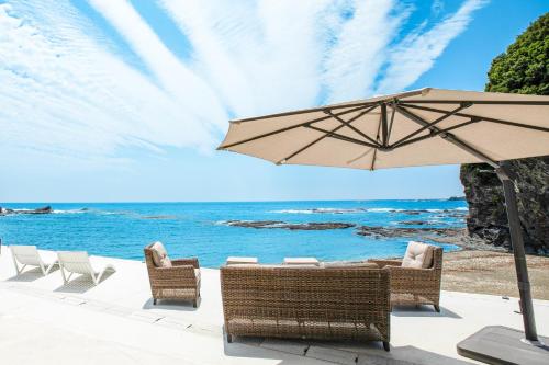 a patio with an umbrella and chairs and the ocean at 熊野古道ビーチテラス串本 in Wabuka