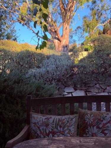 a wooden bench with two pillows on it next to a tree at Barossa Valley’s Captain Rodda’s Cottage in Angaston