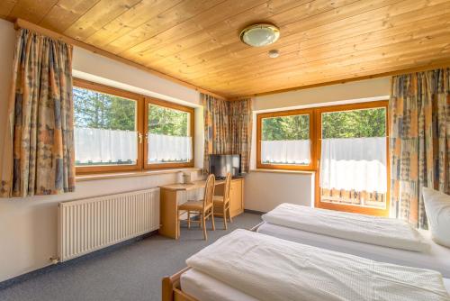 a bedroom with two beds and a desk and two windows at Pension Sattelkopf in Sankt Anton am Arlberg