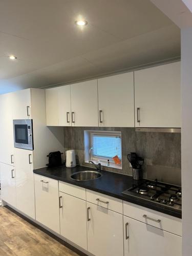 a kitchen with white cabinets and a sink at Luxe Chalet Inn Otterlo op de Veluwe aan het Water! in Otterlo