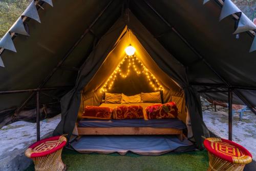 a bed in a tent with two chairs at Himtrek Riverside Camps, Kasol in Kasol