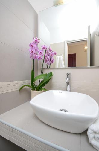 a white bathroom with a sink and a vase of flowers at Perla Hotel in Agios Prokopios