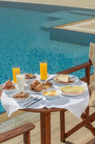a table with breakfast food on a table by a pool at Perla Hotel in Agios Prokopios