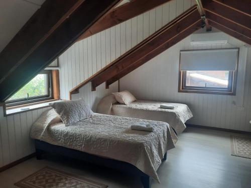 a attic room with two beds and two windows at Cabañas Entre Cerros y Ríos in Futaleufú