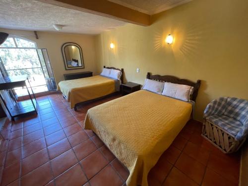a hotel room with two beds and a chair at Hotel Los Arcos in Tlalpujahua de Rayón
