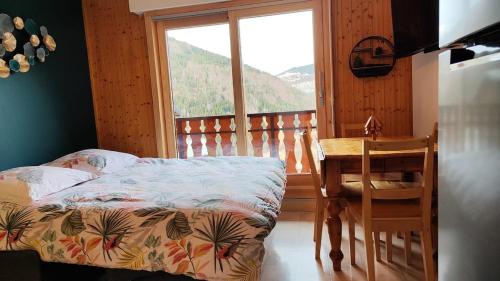 a bedroom with a bed and a table and a window at Chez Nathalie - Appartement cosy- Multi pass offert- Draps, serviettes et ménage compris in Saint-Jean-d'Aulps