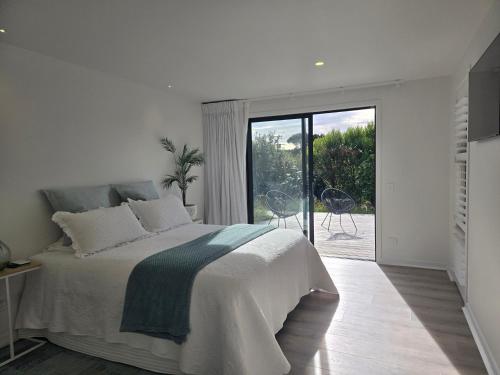 a white bedroom with a bed and a sliding glass door at Pakawau Princess in Pakawau