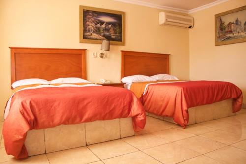 duas camas com capas vermelhas num quarto de hotel em Hotel Posada del Sol Inn em Torreón