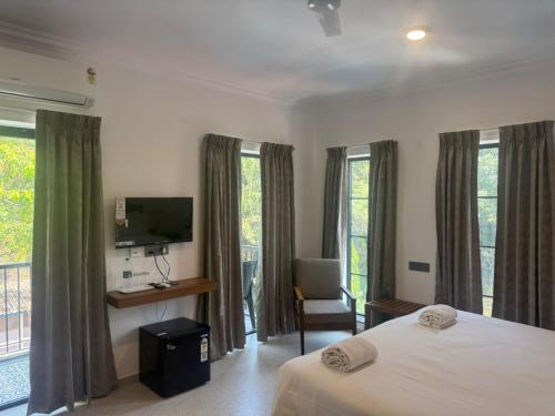 a bedroom with a bed and a tv and windows at Henmil Hideaway in Anjuna
