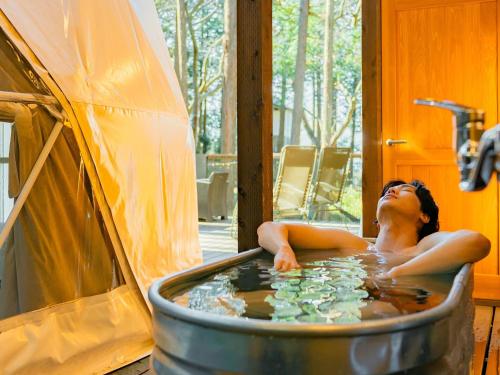 a woman laying in a hot tub next to a tent at エメラルドの森 in Izunokuni