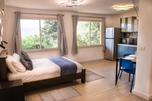a bedroom with a bed and a desk and two windows at הבית ליד הבוסתן דירה לזוג in Mikhmannim