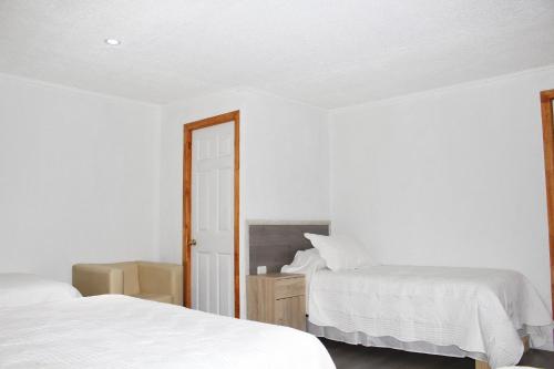 a white bedroom with two beds and a mirror at Residencial Victoria Said in Linares