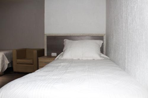 a white bed in a room with a chair at Residencial Victoria Said in Linares