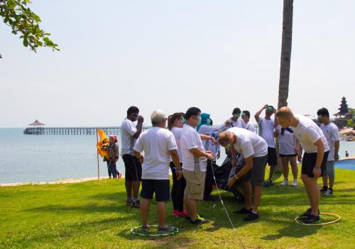a group of people standing on the grass near the water at Turi Beach Resort in Nongsa