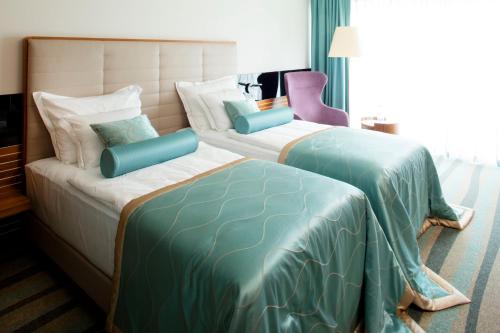 two beds in a hotel room with blue and green sheets at Hotel Navis in Orašje