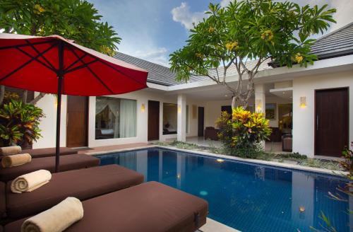 a pool with chairs and an umbrella next to a house at The Yubi Boutique Villas Seminyak - CHSE Certified in Seminyak
