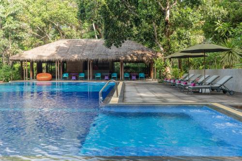 a swimming pool with a hut with chairs and an umbrella at River Kwai Resotel in Sai Yok