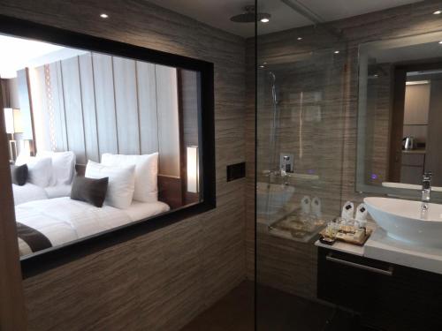 a bathroom with a mirror with a bed and a sink at Arte Hotel - SHA Extra Plus in Bangkok