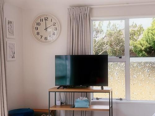 a television on a table next to a window with a clock at Cozy & Sunny Room-Near City, Short Drive to City Center & Coast in Christchurch