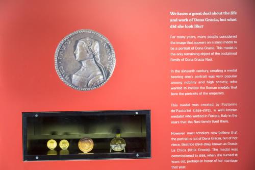 a museum exhibit with coins on a red wall at Hotel & Museum Dona Gracia in Tiberias