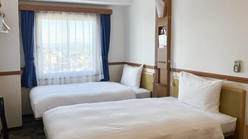 two beds in a hotel room with a window at Toyoko Inn Oita Nakatsu Ekimae in Nakatsu