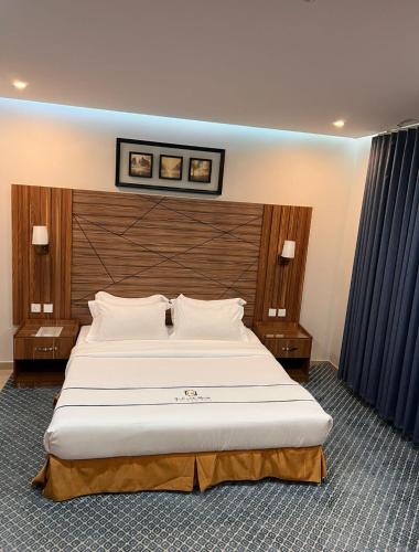 a bedroom with a large white bed with a wooden headboard at رندة المدن للشقق المخدومة in Jazan