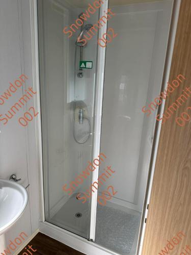 a shower with a glass door next to a sink at Snowdon Summit 002 in Barmouth