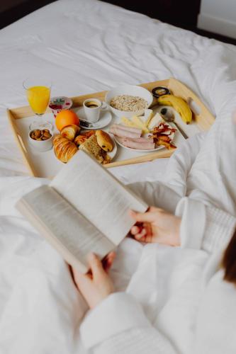 une femme allongée dans son lit avec un plateau de nourriture dans l'établissement Hotel Bloom, à Caen
