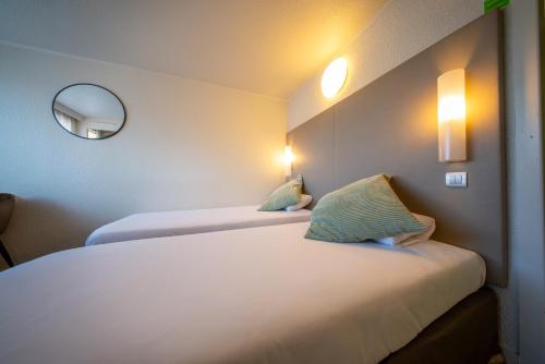 a hotel room with two beds and a mirror at Brit hôtel confort Ampaline Périgueux est in Boulazac