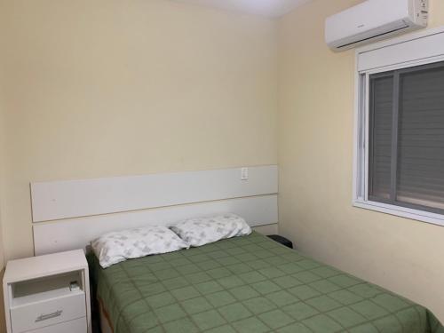 a small bedroom with a green bed and a window at Apartamento junto mar, bem ventilado e iluminado - Antilhas 679 in Capão da Canoa