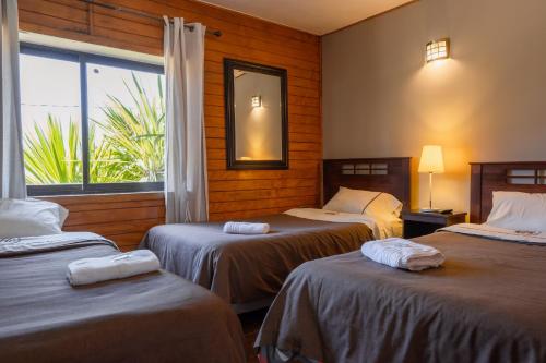 a hotel room with three beds and a window at Hotel de la Costa in Talcahuano