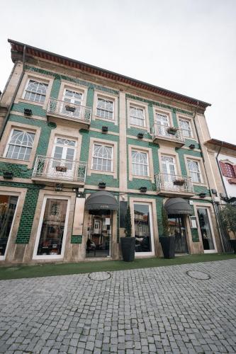 a green building with white windows and a cobblestone street at Santo Thyrso Villas in Santo Tirso