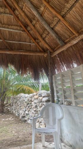 a white chair sitting under a straw roof at Cabañas Puertas del Sol in Telchac