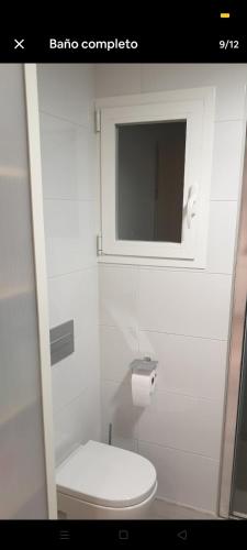 a white bathroom with a toilet and a window at Como en tu casa in Zaragoza