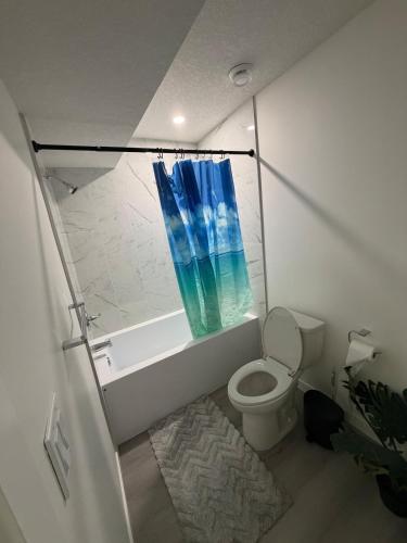 a bathroom with a toilet and a shower with a blue curtain at Brand New 1 Bedroom Basement Suite in Southwest in Edmonton