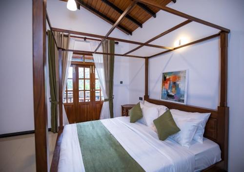 a bedroom with a canopy bed with white sheets and green pillows at Villa Freedom Hikkaduwa in Hikkaduwa