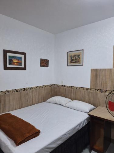 a bedroom with a bed and a table and two pictures at Casa com ar condicionado in Lauro de Freitas