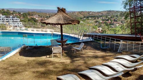 einen Pool mit Stühlen, einem Sonnenschirm und einem Tisch in der Unterkunft Hotel El Faro in Villa Carlos Paz