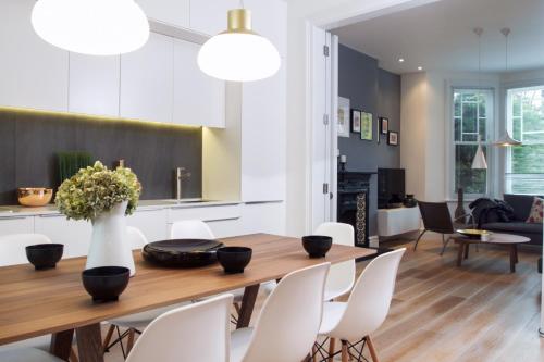 comedor y sala de estar con mesa de madera y sillas blancas en STUNNING Brand New Apartment en Londres