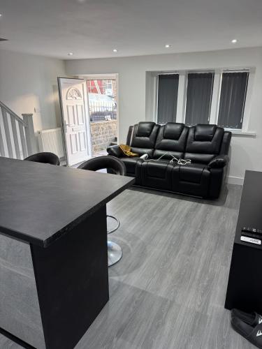 a living room with a black leather couch and a table at Aurang House, 1 Bedroom, with Kitchen, 55" Flat TV, Private Parking in Huddersfield