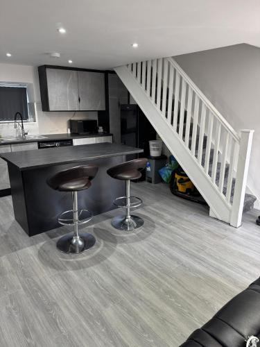 a kitchen with two bar stools and a staircase at Aurang House, 1 Bedroom, with Kitchen, 55" Flat TV, Private Parking in Huddersfield