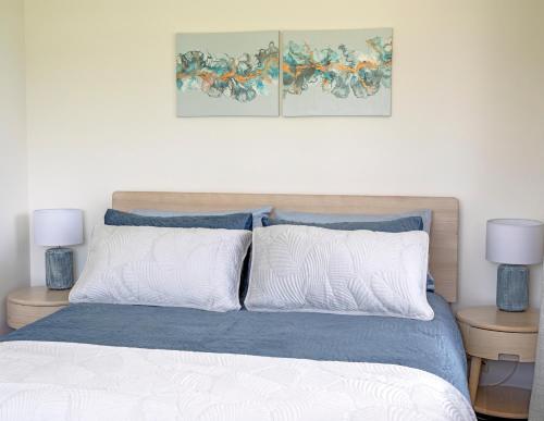 a bedroom with a bed with blue and white sheets and two lamps at Glenmohr Cottage in Waipu