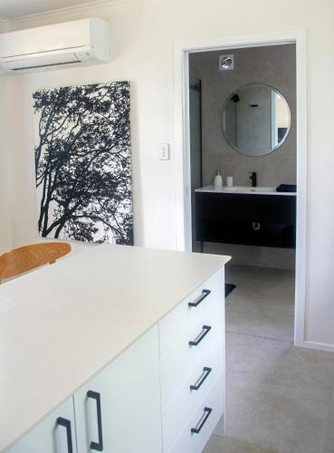 a white bathroom with a sink and a mirror at Glenmohr Cottage in Waipu