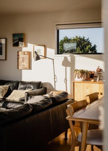 a living room with a black leather couch and a table at Moonbird Beach Shack ~ Ocean Escape in Beaumaris Tasmania