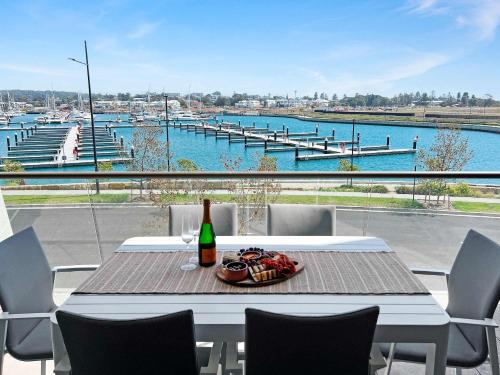 a table with a bottle of wine on a balcony with a harbor at Marina Vista - Waterfront Apartment in Shellharbour