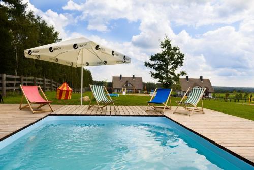a swimming pool with two chairs and an umbrella at Szelągówka Camping&Apartments in Sorkwity