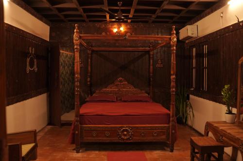 a bedroom with a wooden bed with red sheets at Periyaveettil Heritage in Neyyāttinkara