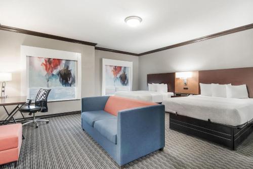 a hotel room with two beds and a blue couch at Hawthorn Suites by Wyndham Lubbock in Lubbock