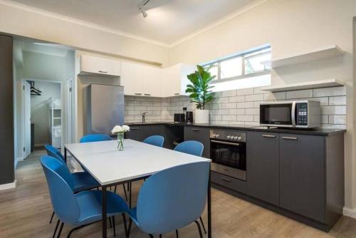 a kitchen with a white table and blue chairs at CURIOCITY Green Point in Cape Town
